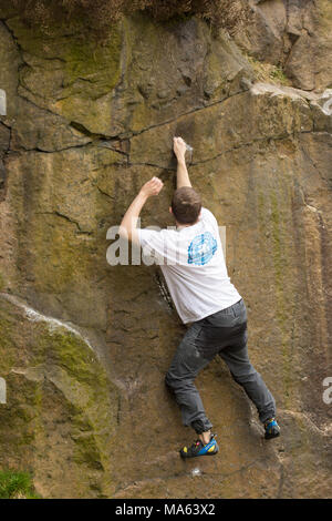 Junger Mann Klettern (Bouldern) ohne Seile auf bräunliche Rock. Stockfoto