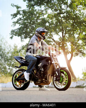 Ternopil, Ukraine - 28. August 2015: junge Biker, Tragen von bunten Helm posiert sitzen auf Sport Motorrad auf sonnigen Stadt Straße. Grüne Pflanzen und Bäume für den Hintergrund. Stockfoto