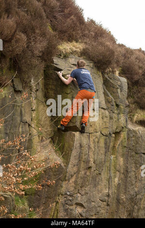 Junger Mann Klettern (Bouldern) ohne Seile auf bräunliche Rock. Stockfoto