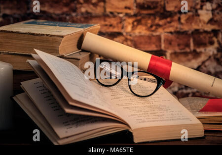 Stapel Bücher mit Origami auf der Oberseite, Kerze, Buch, Notebook, Bleistift und Gläser auf dem Holz braunen Hintergrund gegen alte Mauer Stockfoto