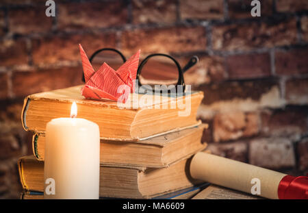 Stapel Bücher mit Origami auf der Oberseite, Kerze, Buch, Notebook, Bleistift und Gläser auf dem Holz braunen Hintergrund gegen alte Mauer Stockfoto