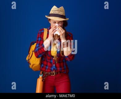 Auf der Suche nach inspirierenden Orten. Kranke reisende Frau in einem Plaid Shirt blasen Nase vor blauem Hintergrund Stockfoto