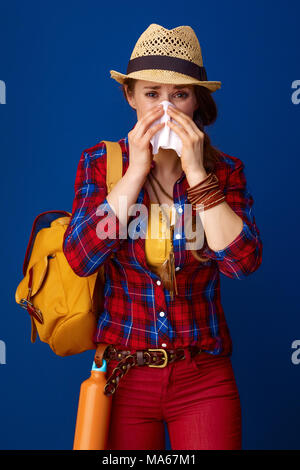 Auf der Suche nach inspirierenden Orten. kranke Frau Wanderer in einen Plaid Shirt blasen Nase isoliert auf Blau Stockfoto
