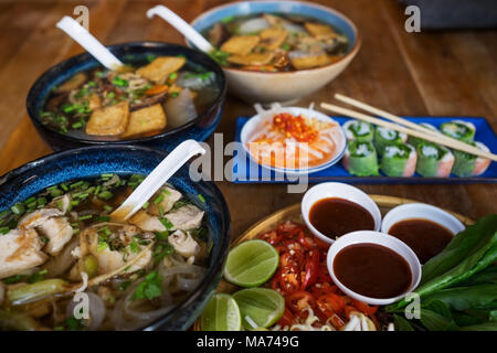 Traditionelle vietnamesische Küche. Suppen, Brötchen und frischen Kräutern. Platten auf einem Holz- Oberfläche. Stockfoto