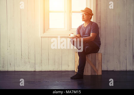 Stattlicher Mann mit den Beinen Kaffee trinken in der Nähe der Fenster gekreuzt Sitzen Stockfoto