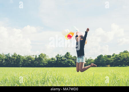 Junge schöne asiatische Frau mit Ballon auf der grünen Wiese laufen und springen frische Luft genießen Stockfoto