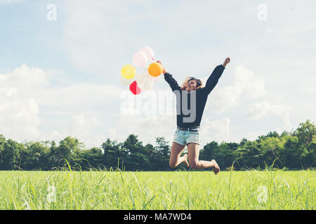 Junge schöne asiatische Frau mit Ballon auf der grünen Wiese laufen und springen frische Luft genießen Stockfoto