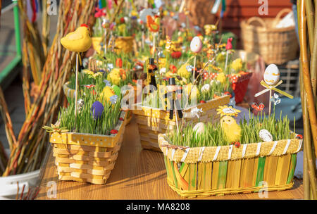 Traditionelle Souvenirs werden auf dem Tisch auf dem Ostermarkt ausgestellt. Holzkörbe mit jungen grünen Getreidesprossen, Ostereier, Ostfiguren Stockfoto