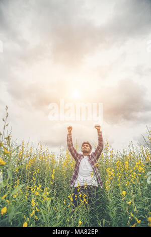 Stattliche hipster Mann, die Hände in die Luft, die in die Gelbe Blume Feld. Stockfoto