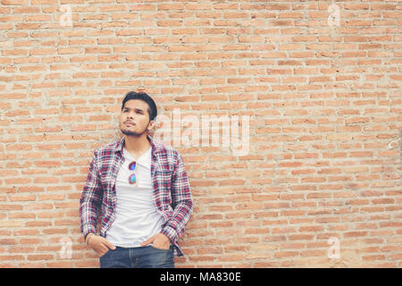 Jungen gutaussehenden Mann, der Coolness Plaid Shirt und Jeans gegen eine Mauer. Stockfoto