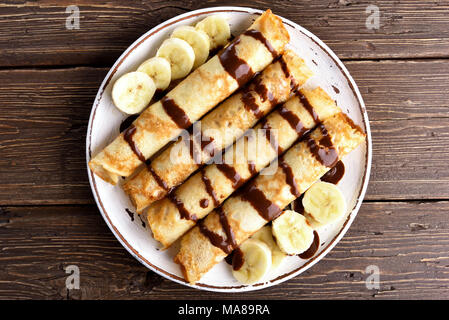 Köstliche Crêpes Rolle mit bananenscheiben auf Holz- Hintergrund. Ansicht von oben, flach Stockfoto