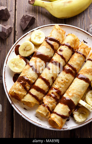 Leckere crepes Rolle mit bananenscheiben auf Holz- Hintergrund. Ansicht von oben, flach Stockfoto