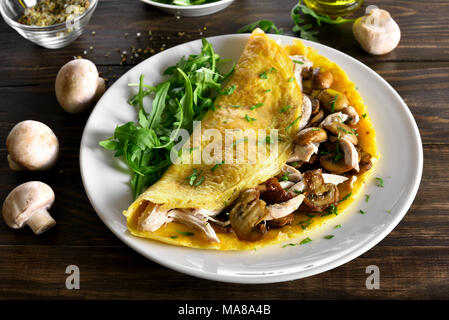 Nahaufnahme von Omelett mit Champignons, Hühnerfleisch, Grüns auf Holztisch. Gesunde Lebensmittel für Frühstück. Stockfoto