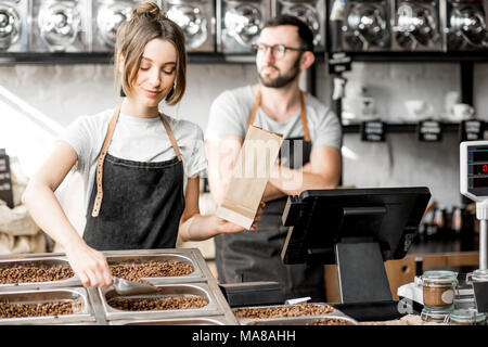 Frau Verkäufer befüllen Säcke aus Papier mit Kaffeebohnen während der Arbeit im Coffee Store Stockfoto