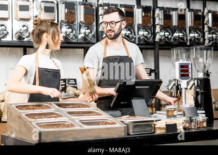 Zwei Verkäufer in Uniform Befüllen von Beuteln mit Kaffeebohnen während der Arbeit im Coffee Store Stockfoto