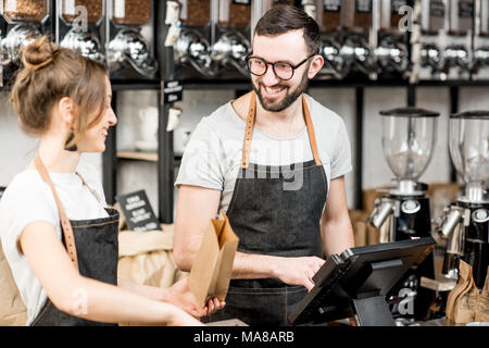 Zwei glückliche Verkäufer in Uniform reden während der Arbeit an der Theke im Coffee Store Stockfoto