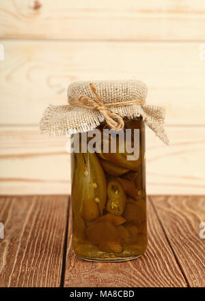 In der Nähe von einem kleinen Glas Glas eingelegte geschnitten Grün hot Jalapeno chili peppers mit Leinwand top Dekoration und Garn auf braunem Holz- Tabelle über Stockfoto