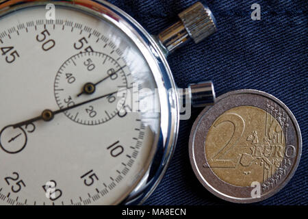 Euro Münze mit einer Stückelung von zwei Euro und Stoppuhr auf dem alten blauen Jeans Hintergrund - Hintergrund Stockfoto