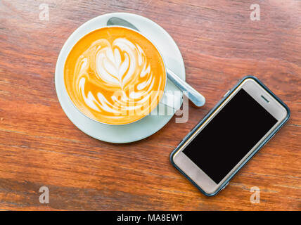 Tasse Latte Art Kaffee mit Smart Phone. Stockfoto