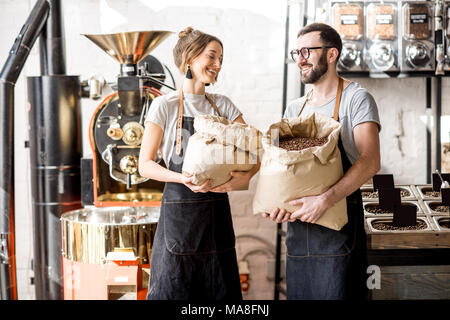 Porträt einer zwei glückliche Baristas in Uniform stehend mit Taschen voller Kaffeebohnen im Coffee Store Stockfoto