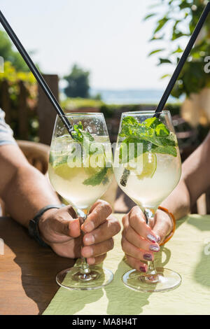 Paar trinken Mojito Cocktails in der gemütlichen Bar im Freien am Strand. Alten männlichen Hand und Hand einer jungen Frau halten die Gläser. Stockfoto