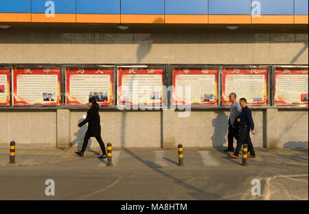 Fußgänger vorbei eine Reihe von Postern an der Wand erklären Aspekte der Governance des Landes im Zentrum von Peking, China Stockfoto