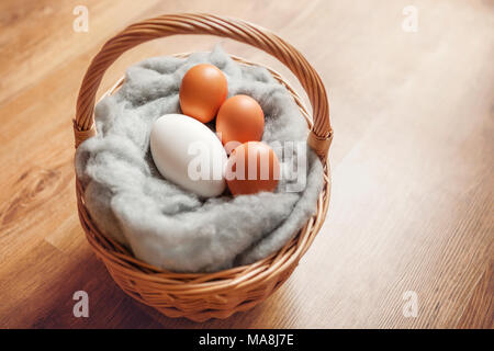 Gänseeier und Hühnereier, in einem Korb auf weicher, flauschiger Wolle, mit einem Holzboden Hintergrund. Stockfoto