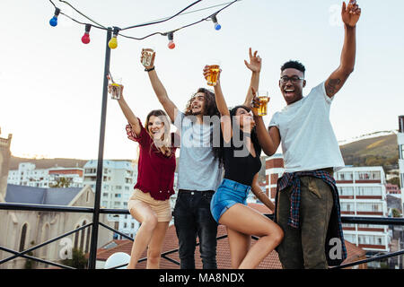 Freunde genießen und Spaß haben auf der Dachterrasse. Multirassischen Männer und Frau, die Party auf dem Dach in Abend. Stockfoto