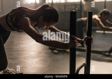 Starke junge Frau Drücken der Schlitten im Fitnessstudio. Frauen, die intensiven körperlichen Training im Fitnessraum. Stockfoto