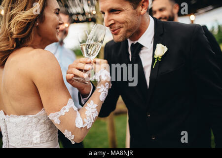 Brautpaar anstoßen und romantische Moment zusammen bei Hochzeit außerhalb. Braut und Bräutigam trinken Champagner in der Hochzeitsgesellschaft. Stockfoto