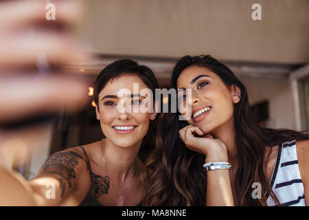 Zwei Frauen sitzen im Freien an einem Handy suchen. Lächelnde Frauen posieren für ein selfie. Stockfoto