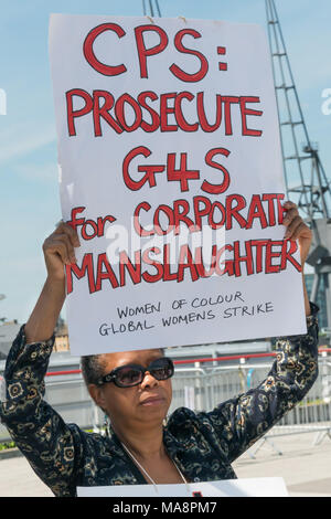 Eine Frau von den Frauen der Farbe in der Globalen Frauen Strik hält ein Poster' CPS: Verfolgung von G4S für Corporate Manslaughter' an der Haltestelle 4S Protest außerhalb G4S AGM am Excel London. Stockfoto