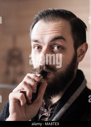 Mann mit Bart und Mustages Vaping eine elektronische Zigarette. Vaper Hipster Rauch Vaporizer im Zimmer. Stockfoto