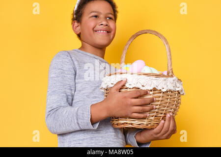 Eine teeneager junge Studio auf gelben Hintergrund Ostern Konzept holding Warenkorb isoliert mit bunten Eiern Unterseite close-up durchführen vorhanden Stockfoto