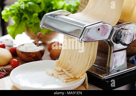 Teig für frische Nudeln und Pasta Maschine am Küchentisch mit Zutaten Stockfoto