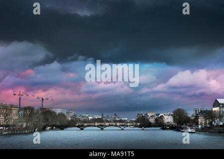 Wabernde Gewitterwolken dunkle und bunte über das Stadtbild sammeln, mit einer geschwollenen Seine und die Pont des Arts Brücke während der Pariser Flut von 2018 Stockfoto