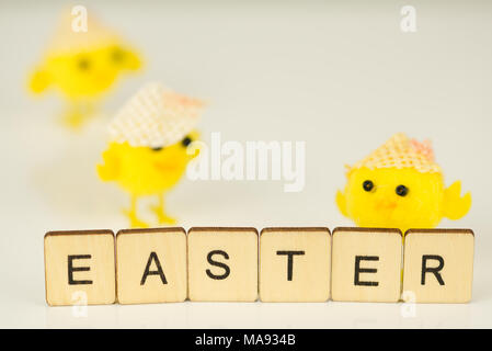 Das Wort Ostern in Brief Fliesen auf weiß reflektierend mit gelben Küken und unscharf im Hintergrund geschrieben. Stockfoto