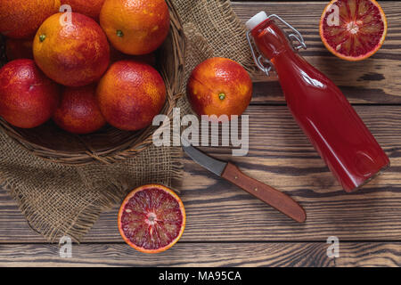 Blut orange Frucht in einem Weidenkorb und Flasche Saft auf dunklen Holztisch. Stockfoto