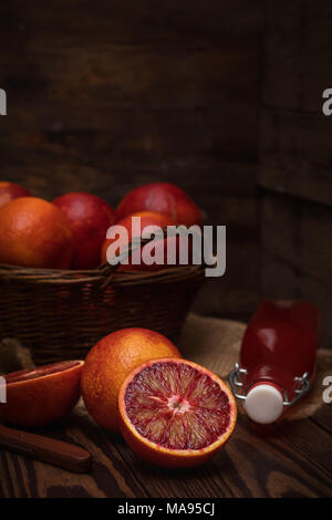 Blut orange Frucht in einem Weidenkorb und Flasche Saft auf dunklen Holztisch. Dunklen rustikalen Stil. Stockfoto