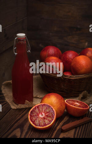 Blut orange Frucht in einem Weidenkorb und Flasche Saft auf dunklen Holztisch. Dunklen rustikalen Stil. Stockfoto