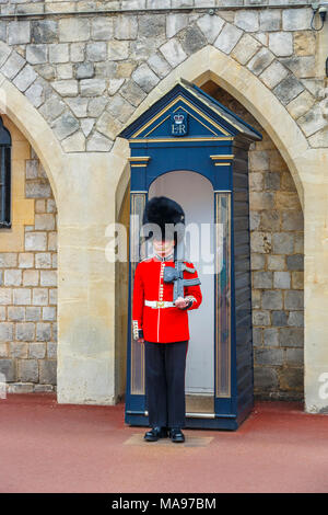 Soldat in der Queen's Guard im Schloss Windsor, England, mit der roten Uniform und traditionellen schwarzen Bärenfellmütze Kappe oder busby ständigen Aufmerksamkeit, Windsor, Großbritannien Stockfoto