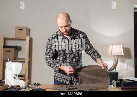 Der Schneider legt die Wolle Gewebe auf dem Schneidwerk. Junger Mann bei der Arbeit als Schneiderin und mit einer Nähmaschine in der Werkstatt. Stockfoto