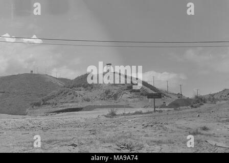 Schwarz-weiß Foto, zeigt eine felsige Landschaft mit einer Straße und Ramada im Mittelgrund und zwei Hügeln im Hintergrund, die jeweils mit einem Holz- Beobachtungsposten auf Gerüsten, in Vietnam während des Vietnam Krieges fotografiert (1955-1975), 1968. () Stockfoto