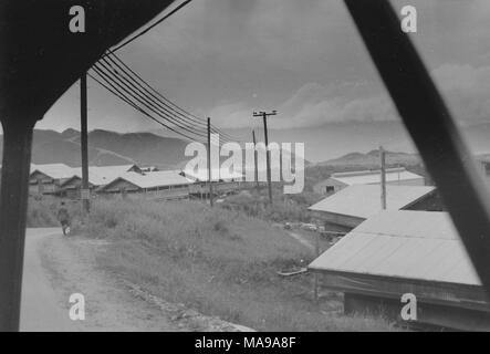 Schwarz-weiß Foto geschossen von im Fahrzeug, von einem Mann auf einem Feldweg, in einem Land, Landschaft, in Kasernen, Telefonmasten bevölkert, und elektrische Pole, in Vietnam während des Vietnam Krieges fotografiert (1955-1975), 1968. () Stockfoto