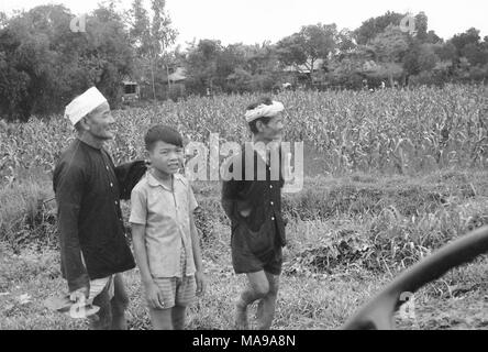 Schwarz-weiß Foto zeigt drei Vietnamesische Männer, ein Junge, kurze Hosen und zwei ältere Männer mit Langarm Shirts, einen Hut tragen, und das andere ein Bandana, vor einem Feld, mit Bäume und Häuser im Hintergrund, die in Vietnam während des Vietnam Krieges fotografiert (1955-1975), 1968. () Stockfoto