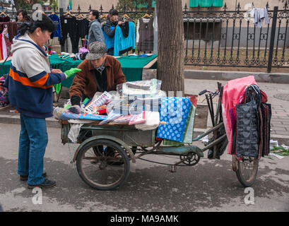 Peking, China - 26. April 2010: Street Market Landschaft, wo Frau Socken kauft von Anbieter mit Dreirad als Schaufenster für den Verkauf von Textilien. Andere Stall mit Clo Stockfoto