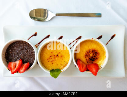 Drei Tassen mit Crème Brûlée, Erdbeeren, und Kakao, serviert auf einem weißen Rechteck Platte. Stockfoto