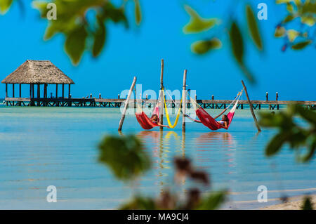 Menschen entspannen in einem roten Hängematten über das Karibische Meer am Strand in Holbox, Mexiko Stockfoto