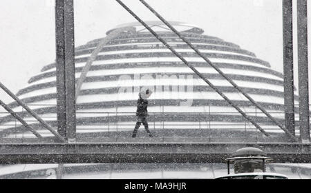 20 März 2018, Deutschland, Berlin: ein Mann gehen unter das Schneetreiben über die Fußgängerbrücke zwischen dem Paul Loebe Gebäude und die Marie Elisabeth Lueders Haus. Der Reichstag Kuppel kann im Hintergrund gesehen werden. Foto: Wolfgang Kumm/dpa Stockfoto