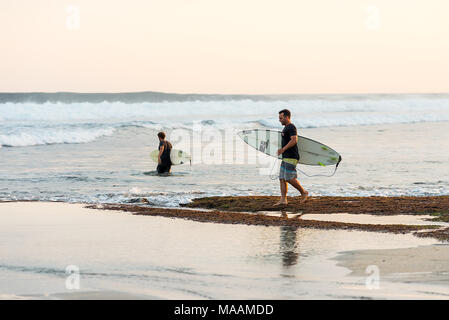 Zwei männliche Surfer Freunde in T-Shirts und Shorts, die surfbretter Kopf vom Ufer in das Südchinesische Meer um Südküste von Sumba Stockfoto